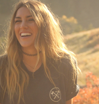 Una donna sorridente in un campo, circondata da elementi naturali.