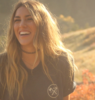 Una donna sorridente in un campo, circondata da elementi naturali.