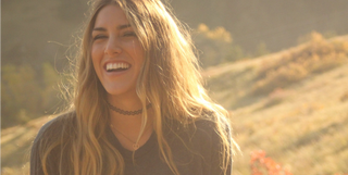 Una donna sorride mentre si trova su una collina, circondata da elementi naturali.