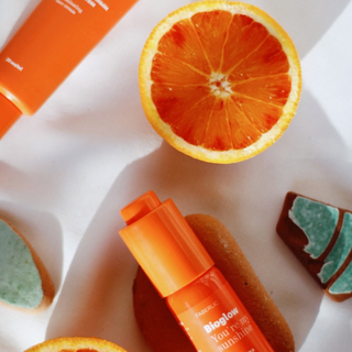 Su un tavolo bianco sono disposti elementi naturali come fette d'arancia e una bottiglia di siero alla Vitamina C.