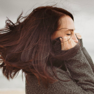 Eine Frau, deren Haare im Wind wehen, umgeben von natürlichen Elementen.