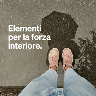 Una persona in jeans e scarpe rosa si trova accanto a una pozzanghera, in cui si riflette un ombrello, con il testo italiano "Elementi per la forza interiore".