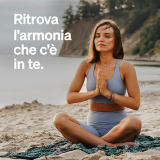 Una donna è seduta a gambe incrociate su una spiaggia, con gli occhi chiusi e le mani in posizione di preghiera. Il testo italiano è: "Ritrova l'armonia che c'è in te."