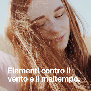 Eine Frau mit langem Haar, das vom Wind geweht wird. Der italienische Text lautet: "Elementi naturali contro il vento e il maltempo.