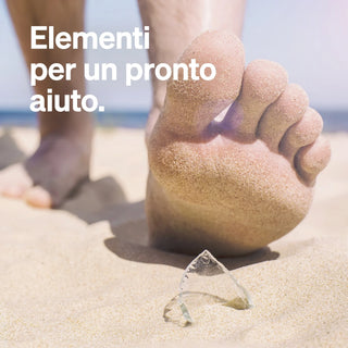 Un piede nudo che calpesta un pezzo di vetro rotto su una spiaggia sabbiosa, con il testo in italiano "Elementi per un pronto aiuto."