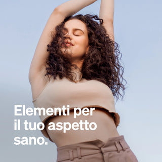 Eine Frau mit lockigem Haar hebt die Arme und schließt die Augen. Sie trägt ein beiges Oberteil und eine Hose. Italienischer Text: "Elementi naturali per il tuo aspetto sano.