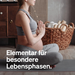 Eine schwangere Frau in grauer Sportkleidung sitzt im Schneidersitz auf einer Yogamatte, die Hände im Gebet. Der deutsche Text lautet: "Elementar für besondere Lebensphasen.