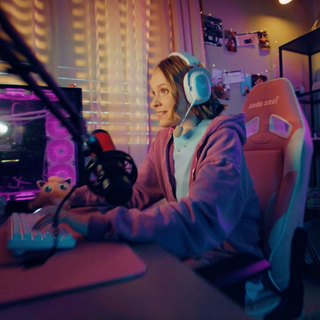 Eine Person, die ein Headset trägt, sitzt in einem Gaming-Stuhl an einem Computertisch mit einem Mikrofon und einer Gaming-Ausrüstung.