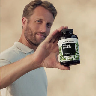 Ein Mann in einem hellen Polohemd hält eine Flasche des Jodergänzungsmittels "Jod aus Bio-Kelp" von Natural Elements hoch und zeigt das Etikett in die Kamera.
