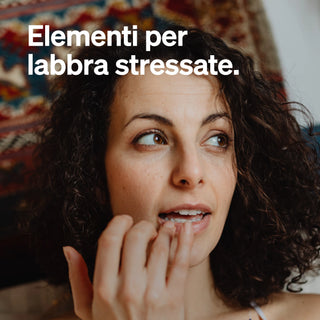 Donna con capelli crespi che si tocca le labbra, con il testo italiano "Elementi per labbra stressate" sovrapposto all'immagine.