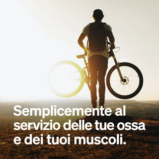 Una persona sta all'aperto al tramonto e tiene con un braccio una bicicletta. Il testo italiano recita: "Semplicemente al servizio delle tue ossa e dei tuoi muscoli.