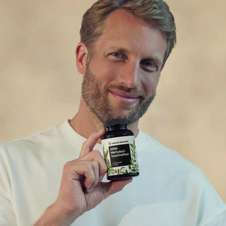 Ein bärtiger Mann mit hellem Haar und weißem Hemd lächelt in die Kamera und hält eine Flasche MSM Methylsulfonylmethan hoch.