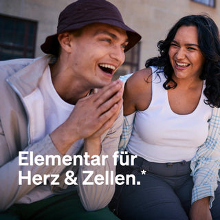 Zwei Menschen sitzen lächelnd und lachend im Freien zusammen. Der Text auf dem Bild lautet: "Elementar für Herz & Zellen.*.