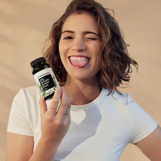 Eine Frau in einem weißen T-Shirt streckt augenzwinkernd ihre Zunge heraus und hält eine Flasche mit der Aufschrift "Epic Brain & Smart Focus" in der Hand.