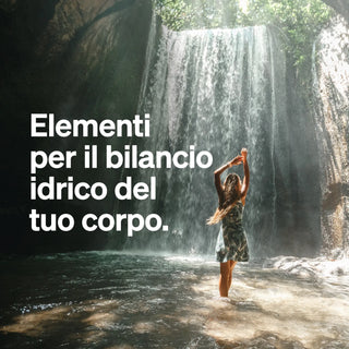 Una donna sta con le braccia alzate in acque poco profonde vicino a una cascata. La luce del sole filtra attraverso gli alberi. Il testo italiano recita: "Elementi per il bilancio idrico del tuo corpo."