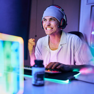 Eine Person, die ein Headset trägt, ballt die Faust und lächelt angestrengt, während sie einen Computer benutzt.
