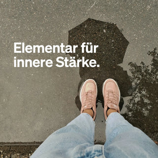 Person in Jeans und rosa Schuhen steht an einer Pfütze und spiegelt einen Regenschirm; deutscher Text: "Elementar für innere Stärke.