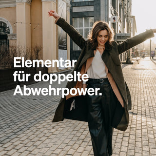 Eine Frau in dunklem Mantel und weiter Hose läuft mit ausgebreiteten Armen. Text: "Elementar für doppelte Abwehrkraft.