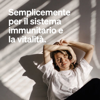 Donna in maglietta bianca seduta a terra con le braccia alzate, occhi chiusi, alla luce del sole. Il testo in italiano promuove il sistema immunitario e la vitalità.