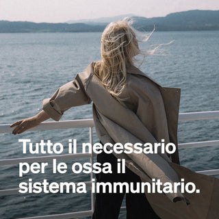 Eine Frau mit langen blonden Haaren in einem beigen Mantel. Italienischer Text über das Wesentliche für Knochen und Immunität, inspiriert von der Natur.