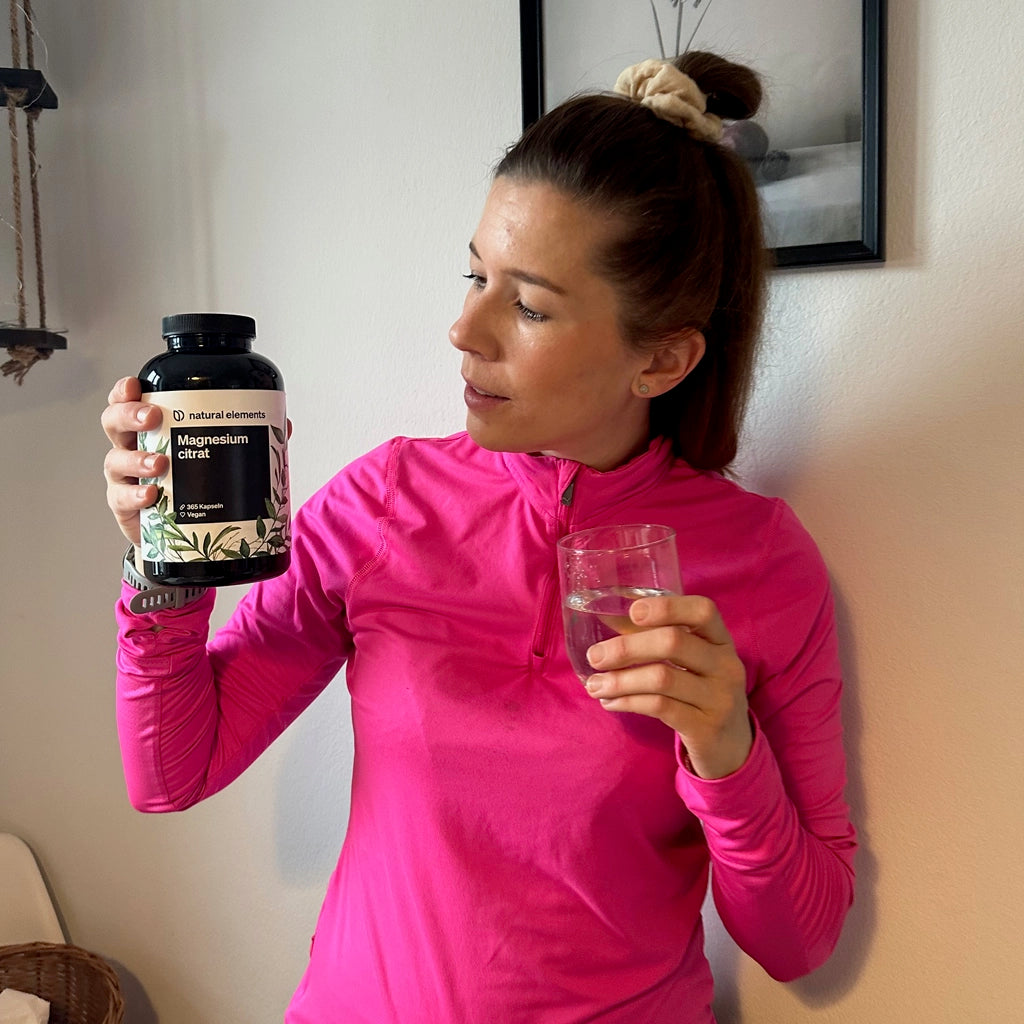 Eine Frau hält eine Flasche Wasser und natürliche Nahrungsergänzungsmittel in der Hand.
