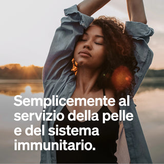 Eine Frau steht mit geschlossenen Augen und erhobenen Armen. Der italienische Text wirbt für die Pflege der Haut und des Immunsystems.